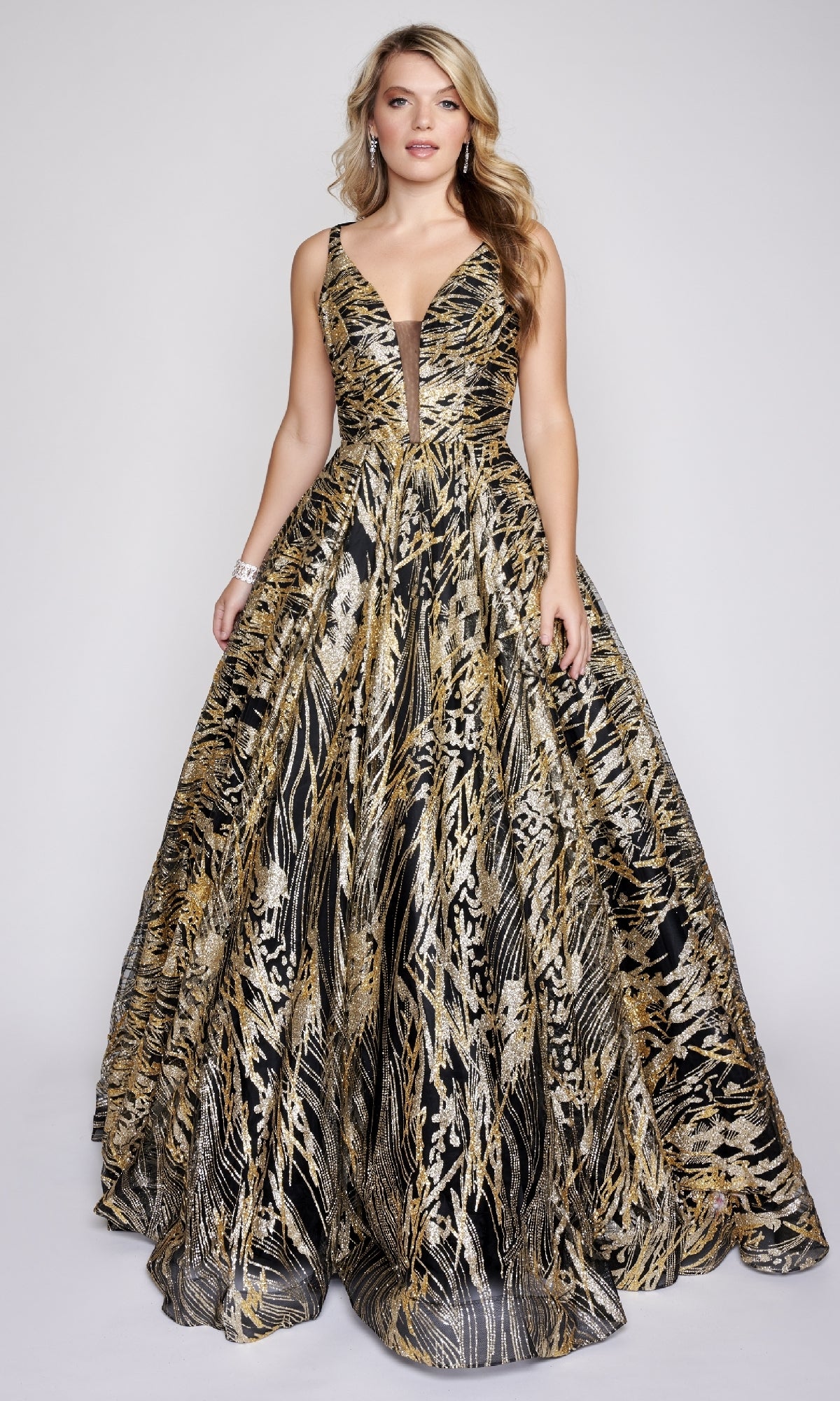 A woman wears the Nina Canacci 8209 Print Prom Ball Gown, a sleeveless, floor-length A-line dress with a black base and detailed gold and silver metallic patterns.